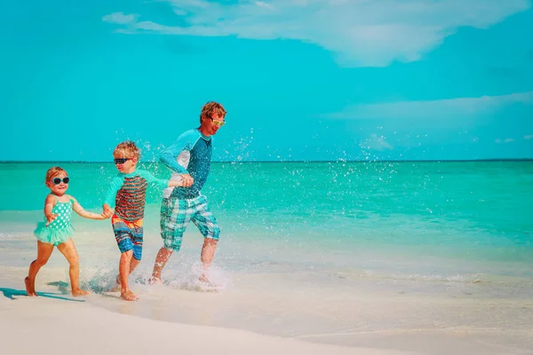 Vader met kinderen spelen met water lopen op strand — Stockfoto