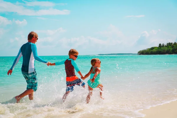 Vader met kinderen spelen met water lopen op strand — Stockfoto