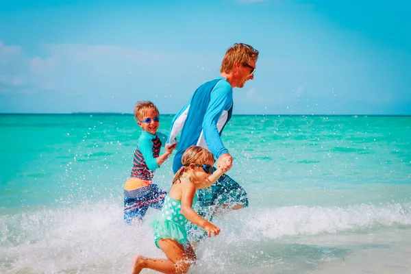 Vader met kinderen spelen met water lopen op strand — Stockfoto