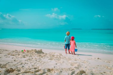 Küçük oğlan ve kız kumsalda kumla oynuyorlar.