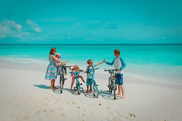 Happy young family with kids riding bikes on beach — Stock Photo, Image
