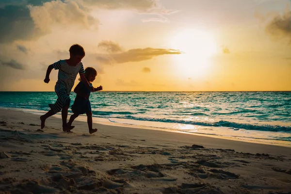 Malý chlapec a dívka se hrají na pláži při západu slunce — Stock fotografie