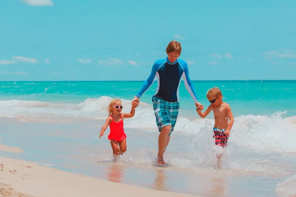 Gelukkige vader met weinig zoon en dochter spelen met water op het strand — Stockfoto