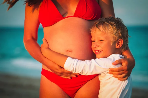 Menino abraçando grávida mãe barriga na praia — Fotografia de Stock