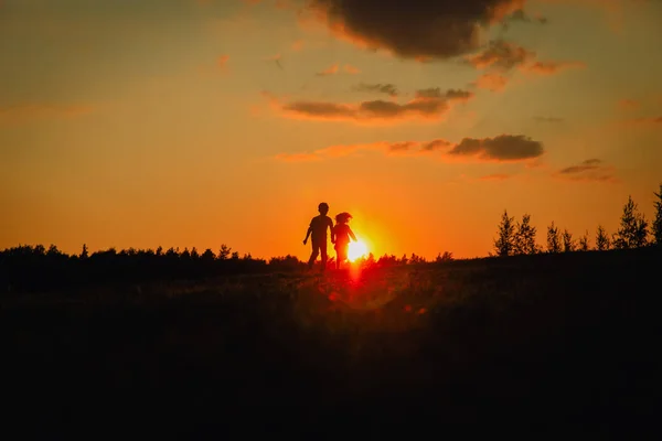 Silhouette de garçon et fille heureux courir dans la nature coucher de soleil — Photo