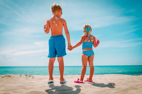 Zonwering, klein meisje en jongen met zonnecrème op het strand — Stockfoto