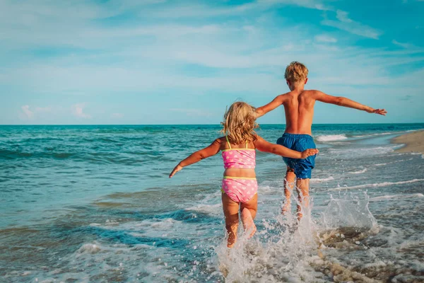 Маленькая девочка и мальчик бегают мухи играть с волнами на пляже — стоковое фото