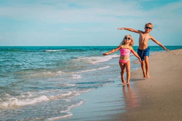 Mutlu küçük kız ve erkek sahilde dalgalar ile oynamak sinek koşmak — Stok fotoğraf