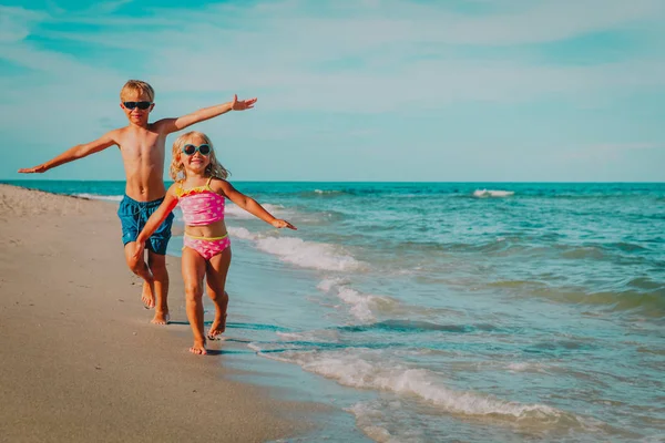 Mutlu küçük kız ve erkek sahilde dalgalar ile oynamak sinek koşmak — Stok fotoğraf