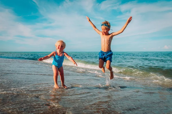 Klein meisje en jongen springen op het strand, kinderen genieten van vakantie op zee — Stockfoto