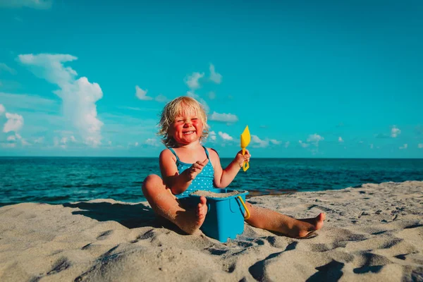 Счастливая милая маленькая девочка играет с песком на пляже — стоковое фото