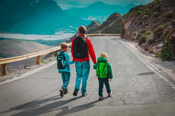 Pai com dois filhos andando na estrada, viajar em montanhas — Fotografia de Stock