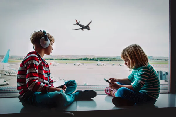 Fiú és lány-val mozgatható telefon és érint egészségügyi betét váró-ban repülőtér — Stock Fotó