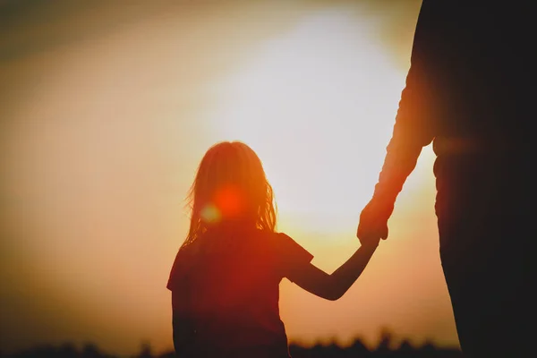 Silueta de niña sosteniendo la mano del padre al atardecer — Foto de Stock