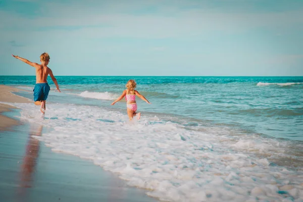 Klein meisje en jongen vliegen lopen spelen met golven op het strand — Stockfoto