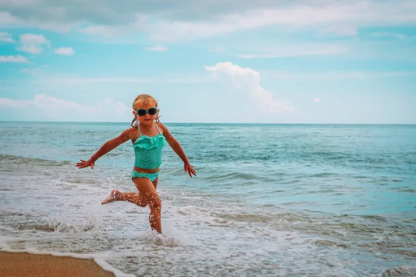 mutlu küçük kız sahilde dalgalar ile oyun koşmak