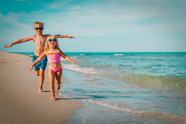 Felice bambina e ragazzo correre volare giocare con le onde sulla spiaggia — Foto Stock