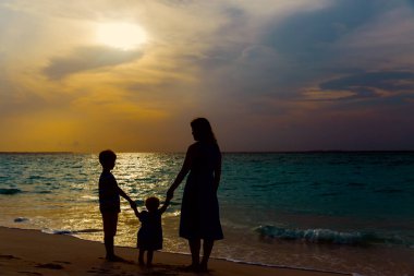 Anne ve iki çocuğu batımında sahilde yürüyüş