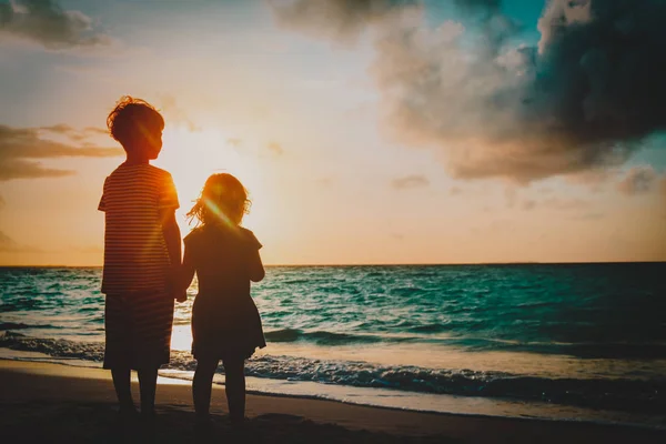 Glad liten pojke och en flicka som håller händerna vid solnedgången — Stockfoto