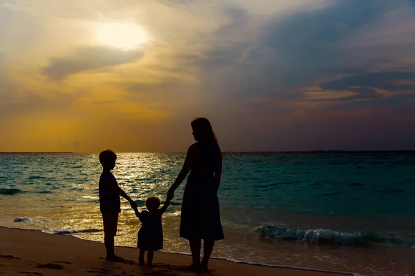 Mãe e dois filhos andando na praia ao pôr do sol — Fotografia de Stock