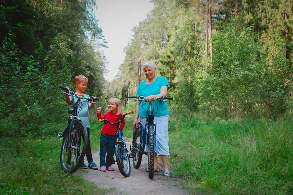 Avó sênior ativo com crianças andar de bicicleta na natureza — Fotografia de Stock