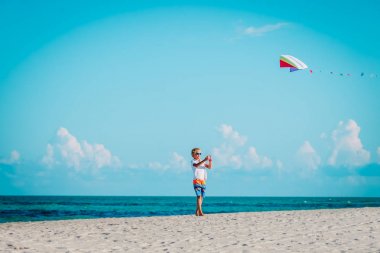 Genç bir çocuk tropik sahilde uçurtma uçuruyor.