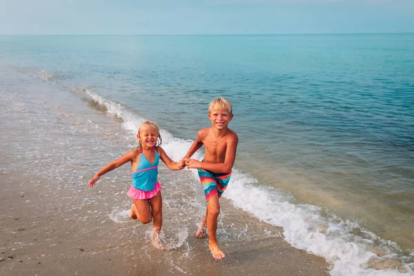 Χαρούμενο κορίτσι και αγόρι τρέχουν να παίξουν με κύματα στην παραλία — Φωτογραφία Αρχείου
