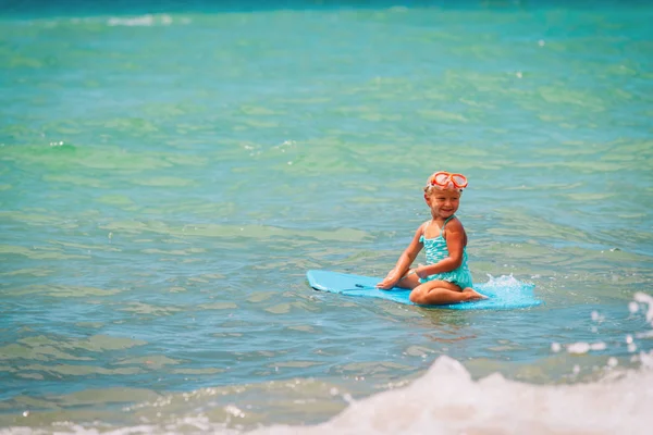 Ευτυχισμένο μικρό κορίτσι παίζουν με σανίδα σερφ στη θάλασσα — Φωτογραφία Αρχείου