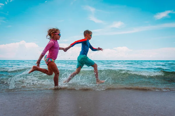 Счастливые девочка и мальчик бегают по пляжу, дети играют с водой в море — стоковое фото
