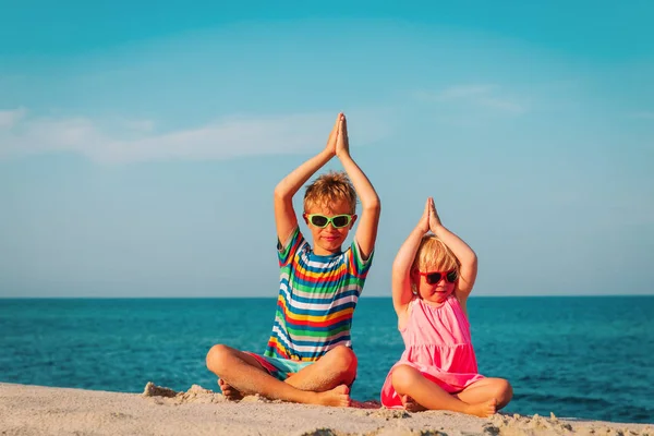 Menino bonito e menina fazendo ioga na praia, exercício das crianças no mar — Fotografia de Stock