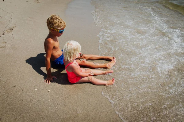 Menino e menina brincam com água nas férias na praia, as crianças relaxam e se divertem — Fotografia de Stock