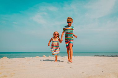 Mutlu çocuk ve kız plajda koşuyorlar.