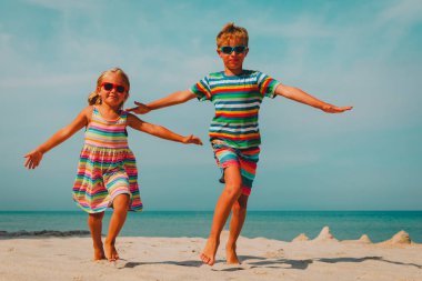 Mutlu çocuk ve kız plajda koşuyorlar.