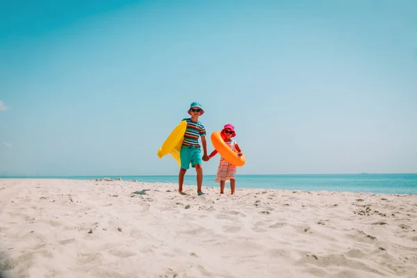 Šťastný děti-chlapec a děvče s floatiemi jdou na pláž — Stock fotografie