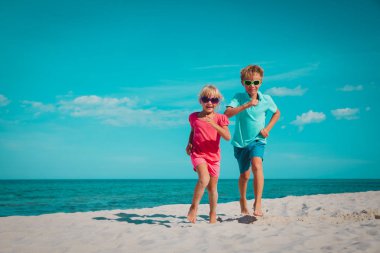 Mutlu çocuk ve kız plajda koşuyorlar.