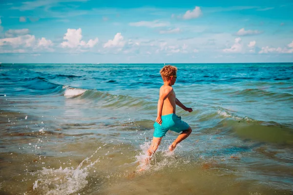 เด็กชายที่มีความสุขวิ่งและเล่นกับน้ําบนชายหาด — ภาพถ่ายสต็อก