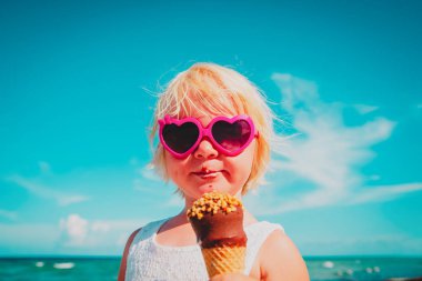 Kumsalda dondurma yiyen mutlu küçük kız.