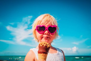 Kumsalda dondurma yiyen mutlu küçük kız.