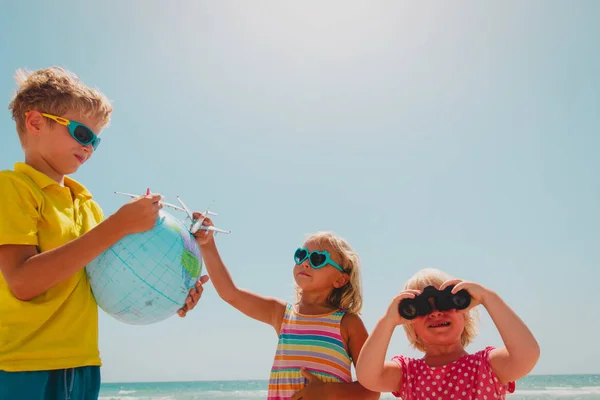 Dzieci podróży na plaży, chłopiec i dziewczęta z globu, zabawki samolotu i lornetki — Zdjęcie stockowe