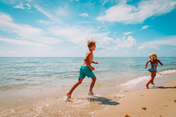 Gelukkige jongen en meisje rennen op het strand, kinderen spelen met water op zee — Stockfoto