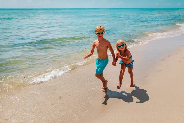 Счастливые маленькая девочка и мальчик бегут на пляже — стоковое фото