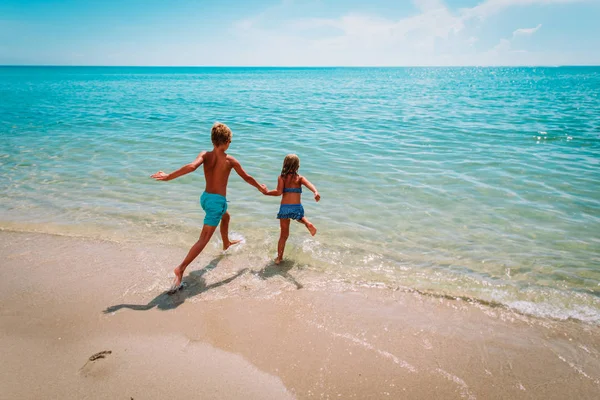 Gelukkige jongen en meisje rennen om te zwemmen op het strand — Stockfoto