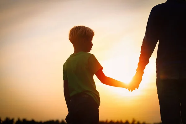 Silhueta de pai e filho de mãos dadas ao pôr do sol — Fotografia de Stock