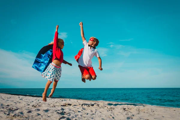 Šťastný chlapec a dívka hrát superhrdinové na pláži dovolenou — Stock fotografie