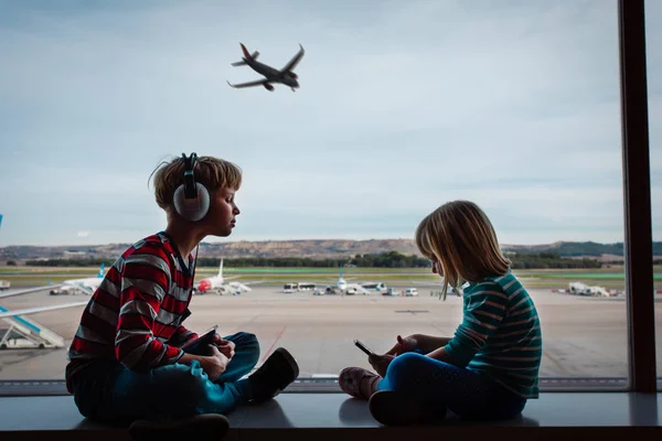 Niño y niña con teléfono móvil y almohadilla táctil esperando en el aeropuerto — Foto de Stock