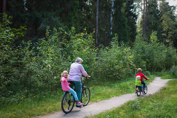 Abuela senior activa con niños montando bicicletas en la naturaleza —  Fotos de Stock