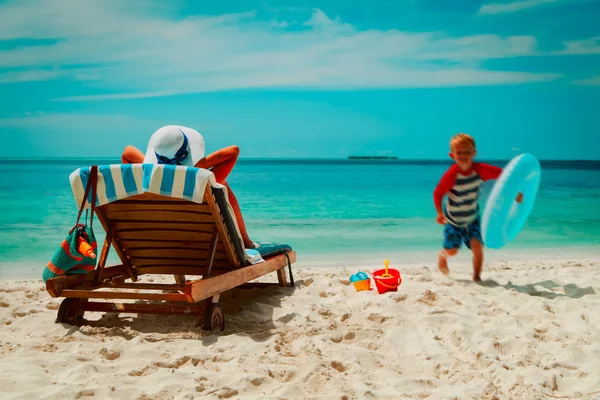 Madre relajarse mientras el niño disfruta jugando en vacaciones en la playa — Foto de Stock