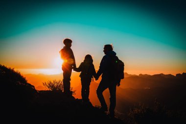 Baba ve kız ve erkek çocukları gün batımında dağlarda geziyorlar.