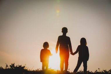 Çocukların siluetleri - erkek ve kız - gün batımında el ele tutuşuyorlar
