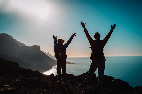 Silhueta de feliz pai e filho viajar em montanhas pôr do sol perto do mar — Fotografia de Stock